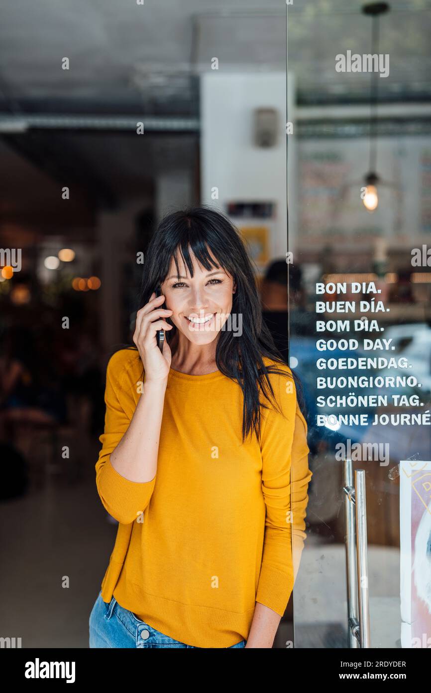 Smiling mature woman talking on mobile phone in cafe Stock Photo