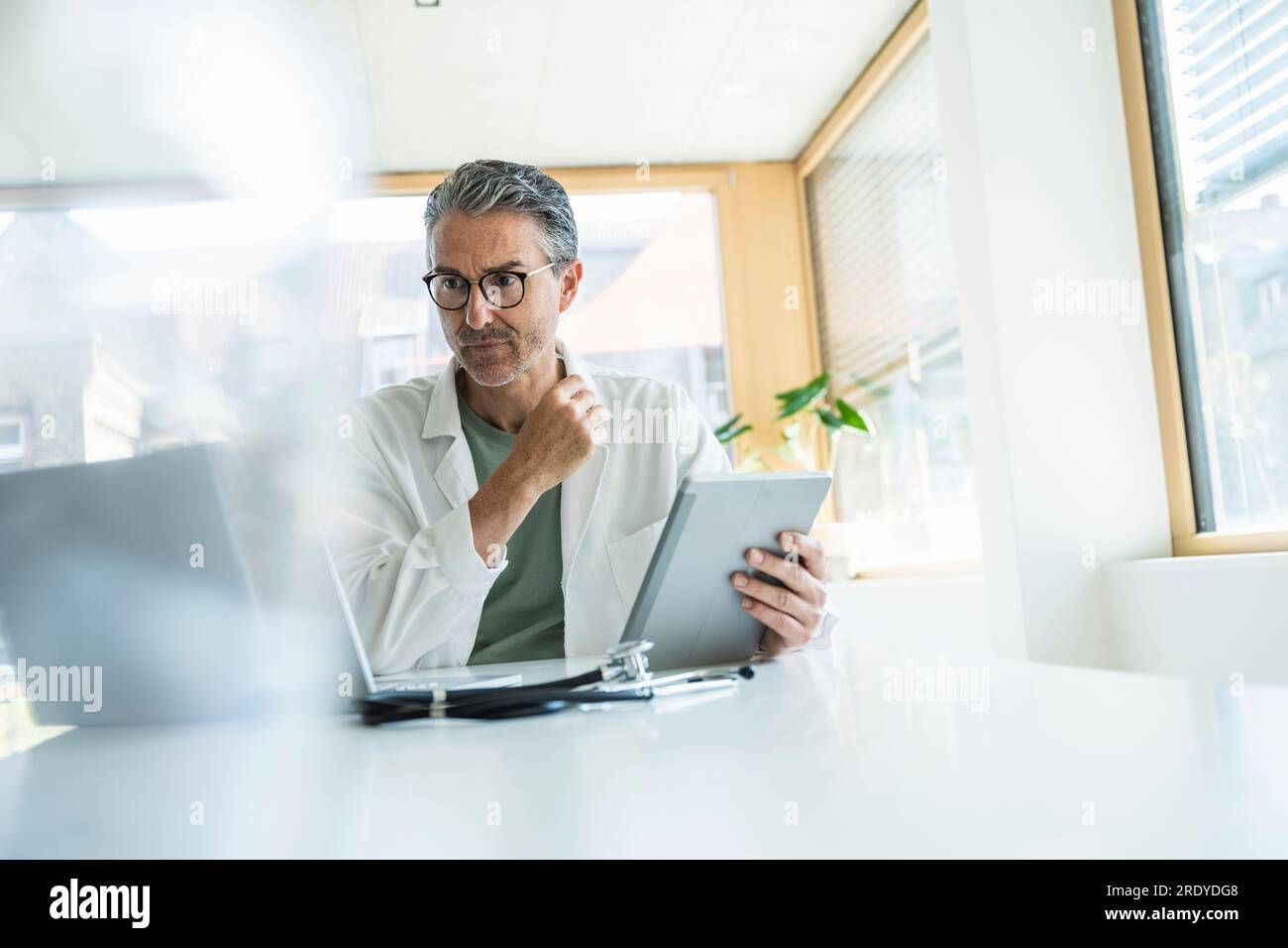 Mature man in lab coat using tablet PC in clinic Stock Photo