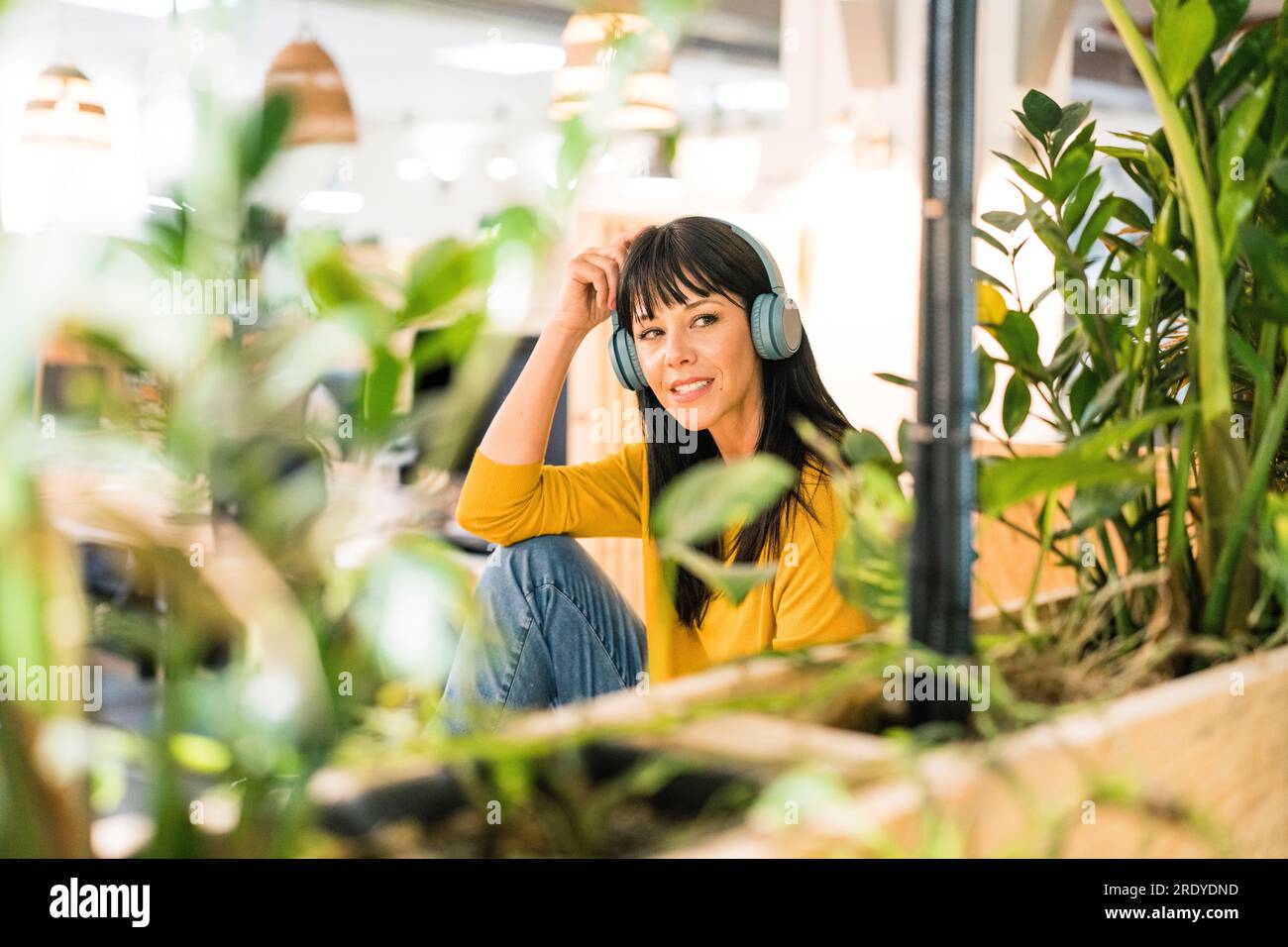 Thoughtful businesswoman wearing wireless headphones sitting in office ...