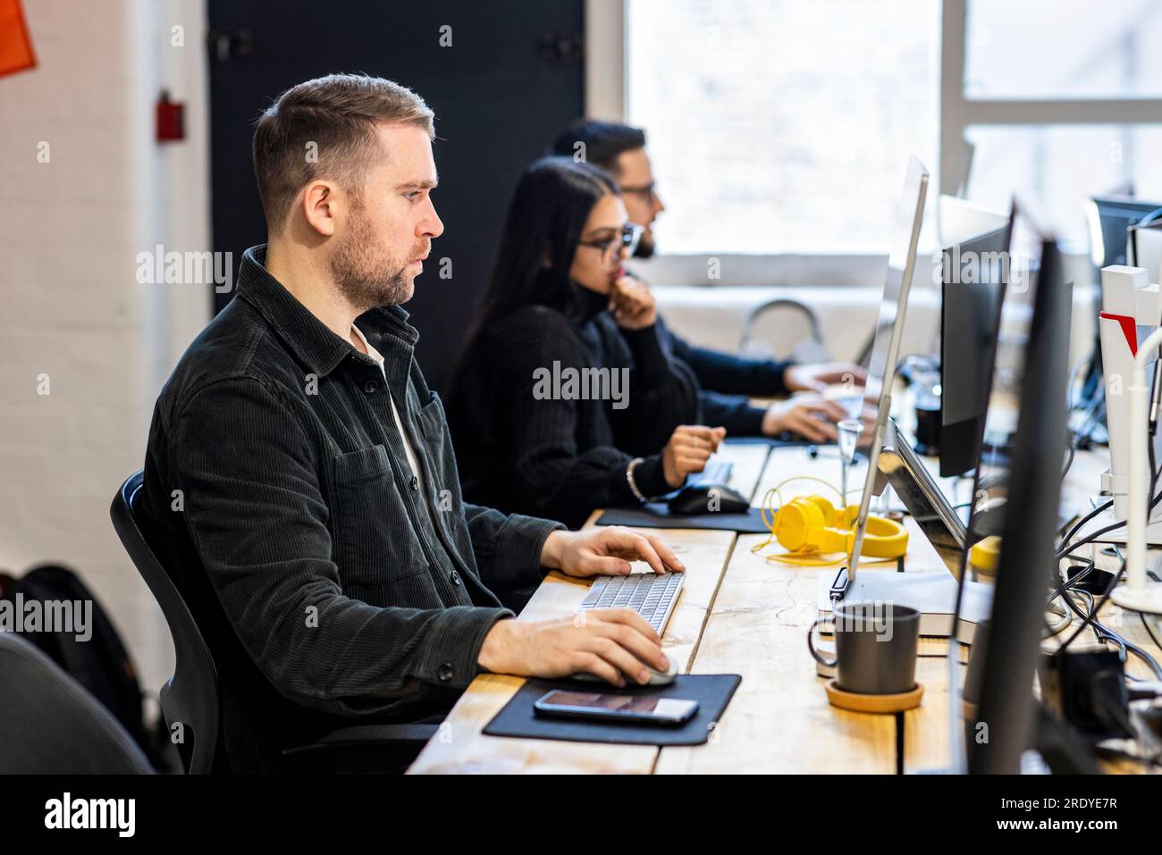 Businessman working on computer with colleagues in background Stock Photo