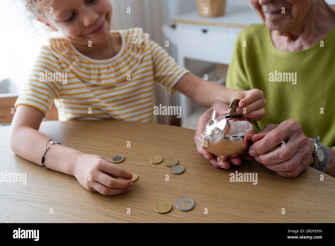 Smiling granddaughter putting coin in piggy bank Stock Photo - Alamy