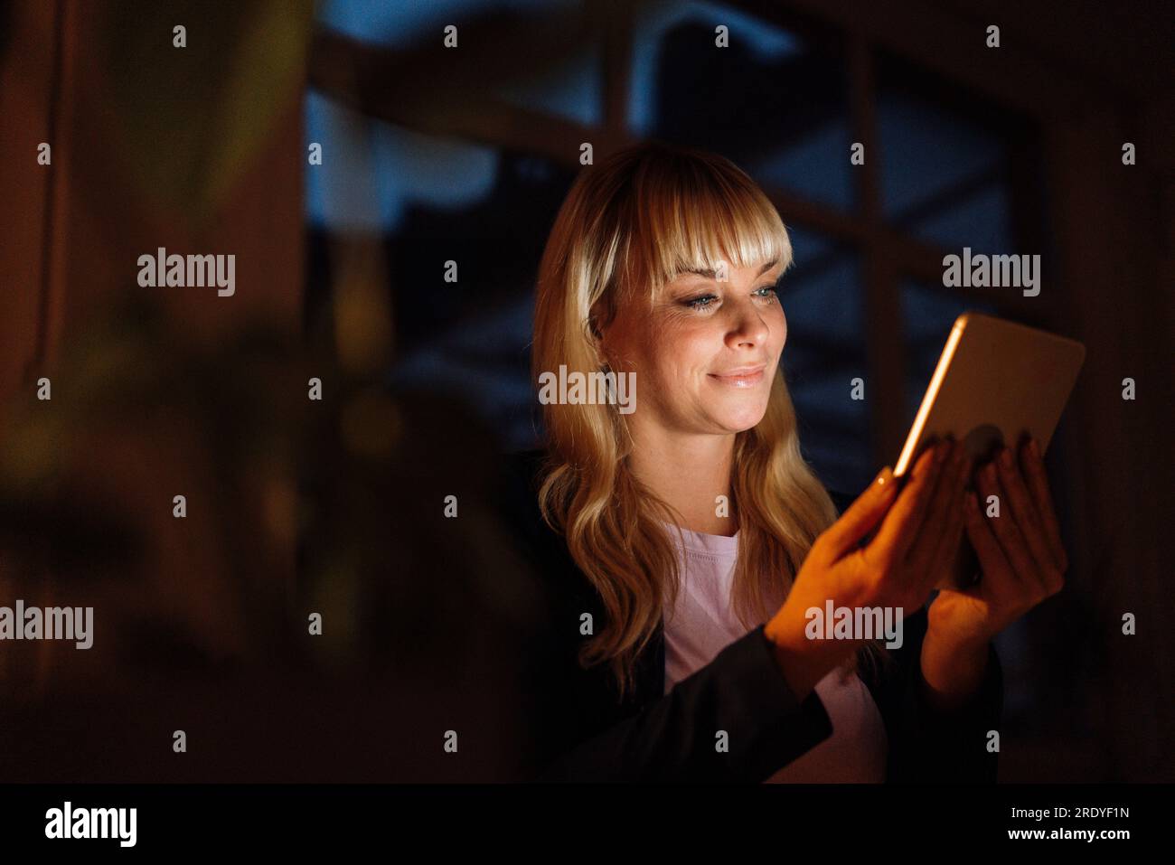 Smiling woman using tablet PC at night Stock Photo