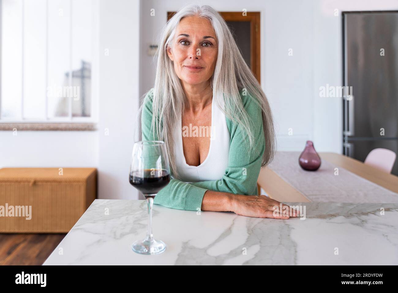 Smiling woman with glass of wine leaning on kitchen island Stock Photo