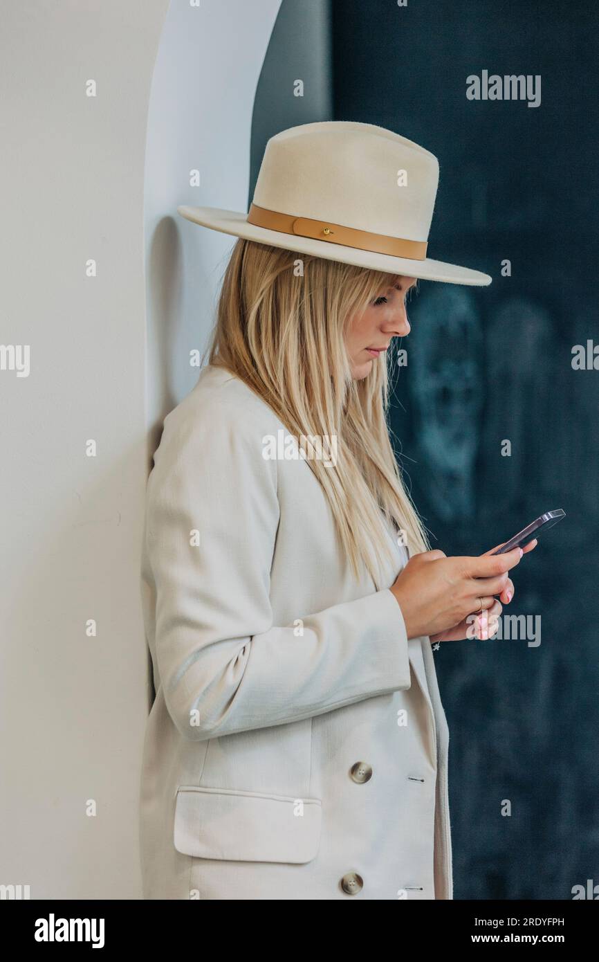 Blond woman using smart phone standing near wall Stock Photo