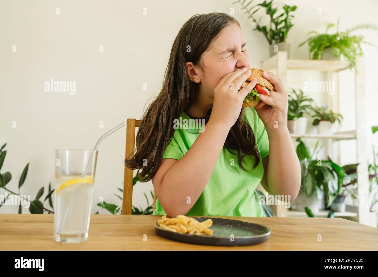 Girl eating hamburger with french fries and soda at home Stock Photo
