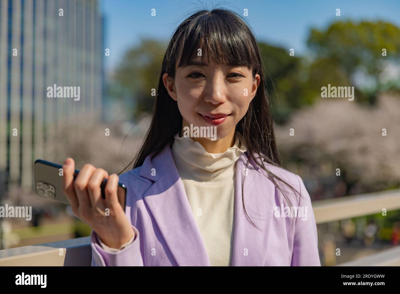 A portrait of Japanese woman with smartphone behind cherry blossom bust ...