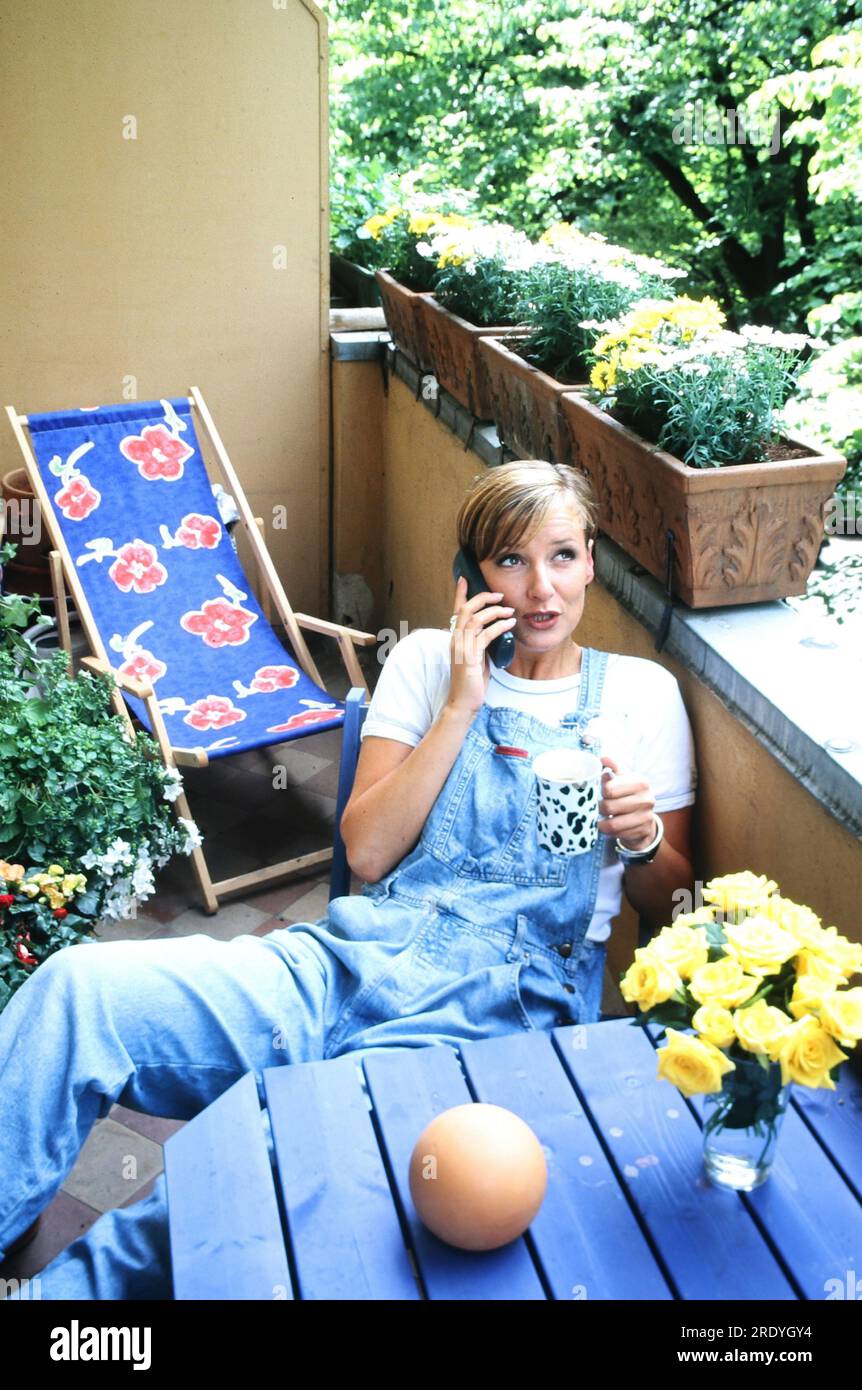 Kim Fisher, deutsche Sängerin, Schauspielerin und Moderatorin, lümmelt sich beim Telefonieren auf dem Balkon während einer Homestory Fotosession in Berlin, Deutschland 1997. Stock Photo