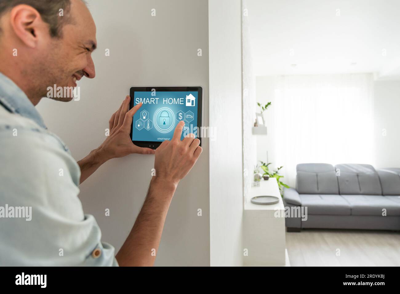 Hispanic man smiling while using his a tablet screen to control his smart home system Stock Photo