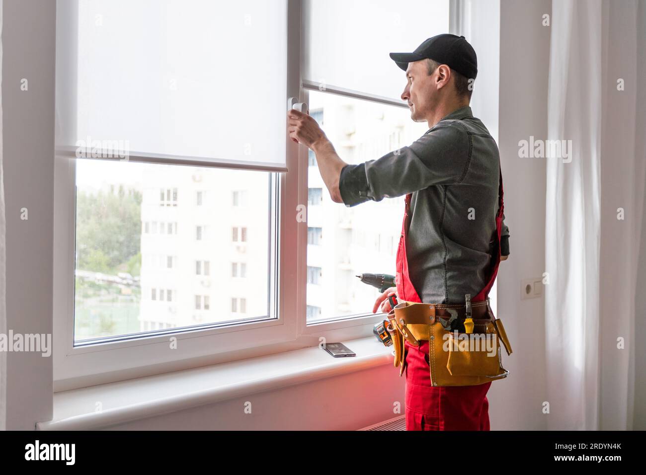 Worker in uniform installing blinds on plastic upvc window. Stock Photo