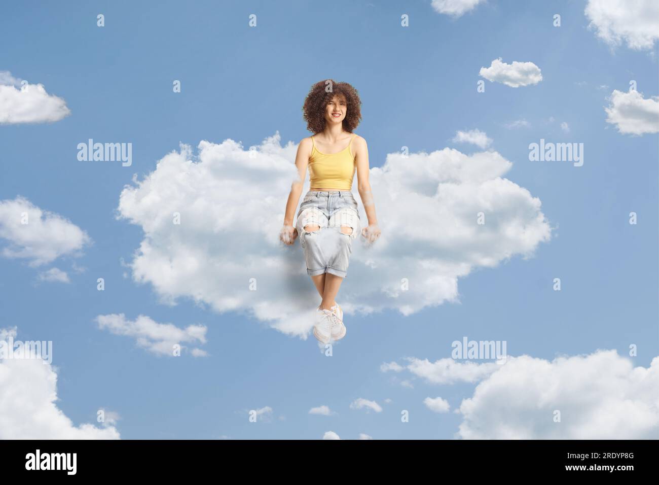 Full length portrait of a young caucasian female with afro hairstyle sitting on a cloud Stock Photo