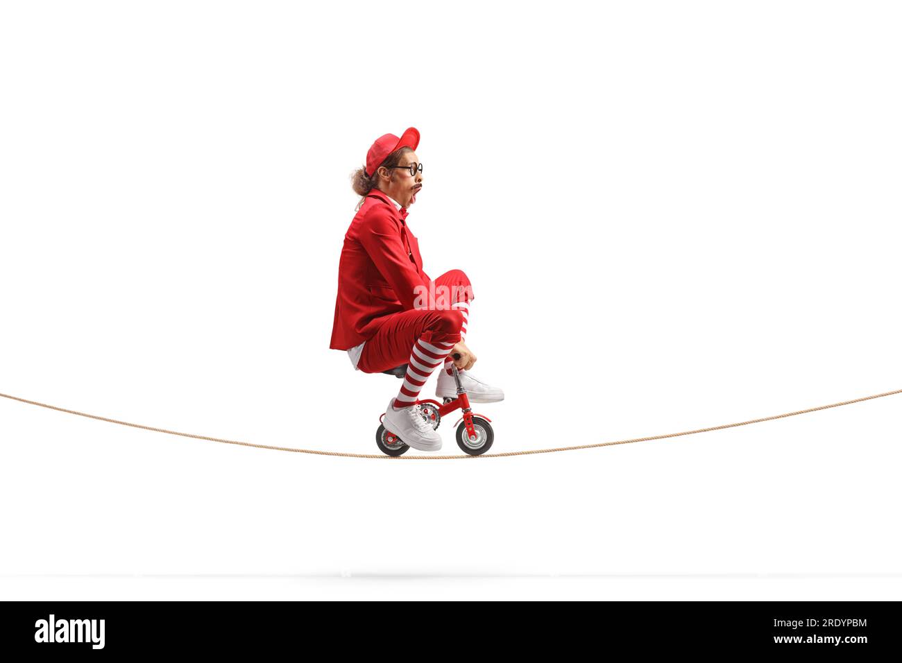 Man in a red suit riding a small red bike on a rope isolated on white background Stock Photo