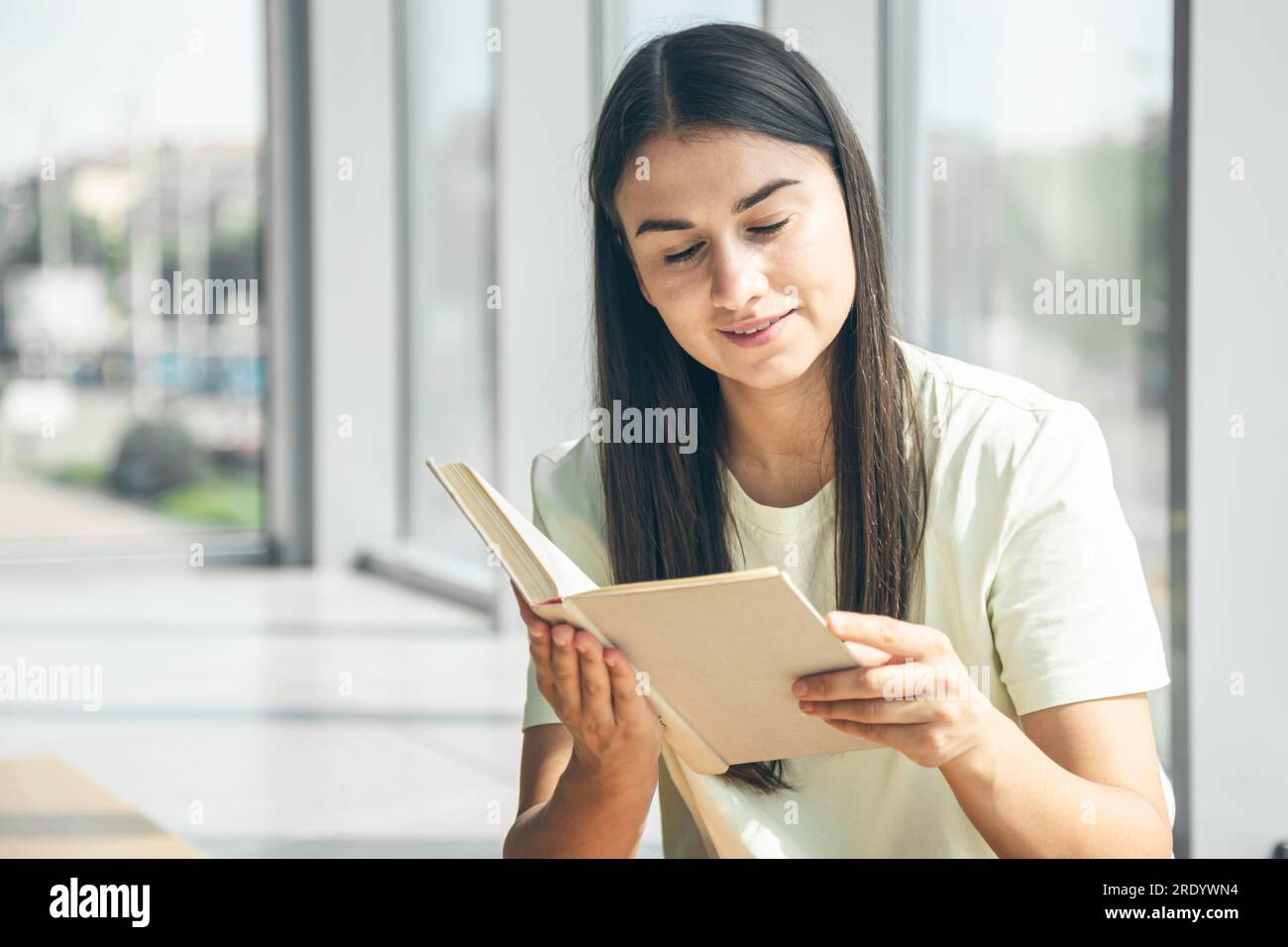 Attractive young woman reads a book while sitting by the window in ...