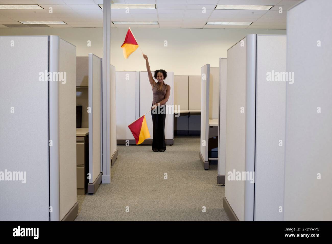 Woman uses semaphore flags to signal coworkers in cubicle-filled office. Stock Photo