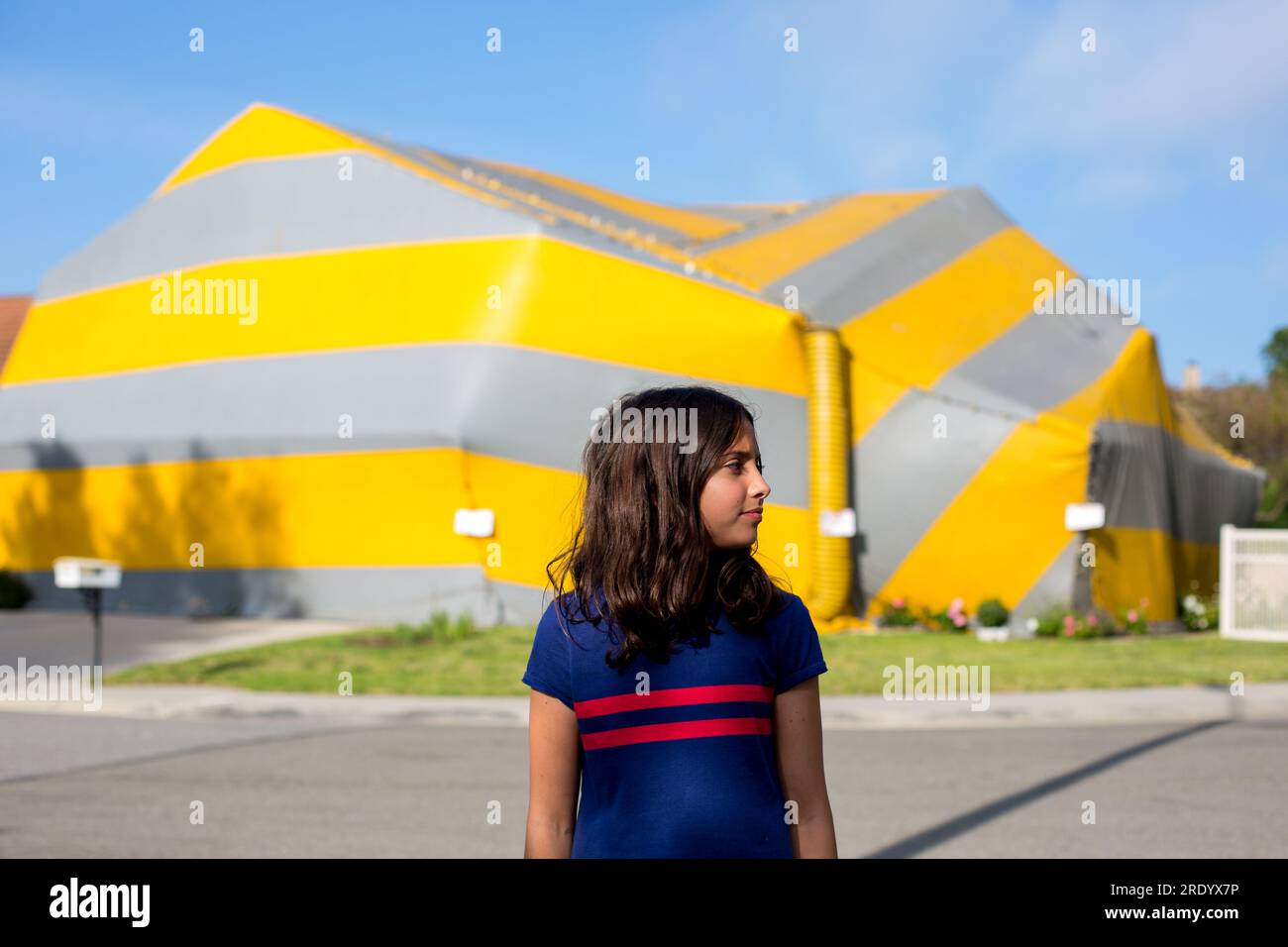 Tented house in background, girl stands outside looking to her left. Stock Photo