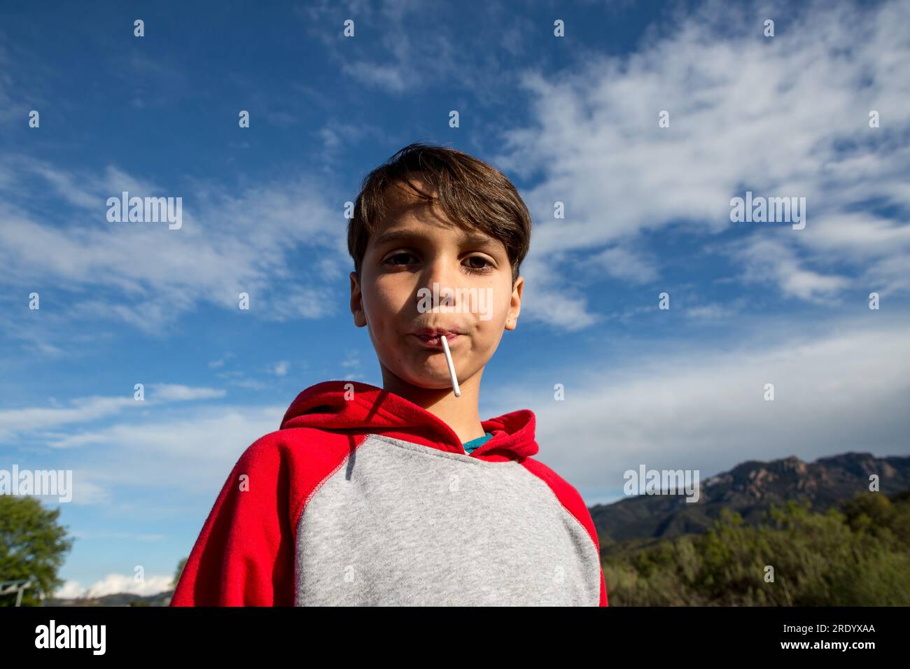 Boy outside looks down at camera with a lollipop in his mouth Stock Photo