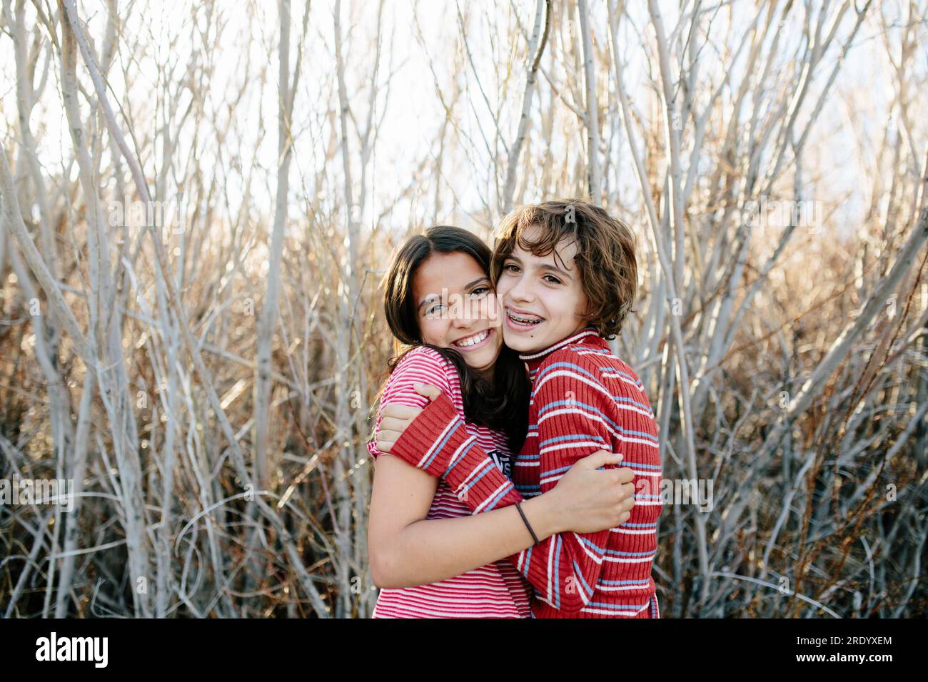 Young teen sisters wearing stripes hug and smile in the woods Stock Photo