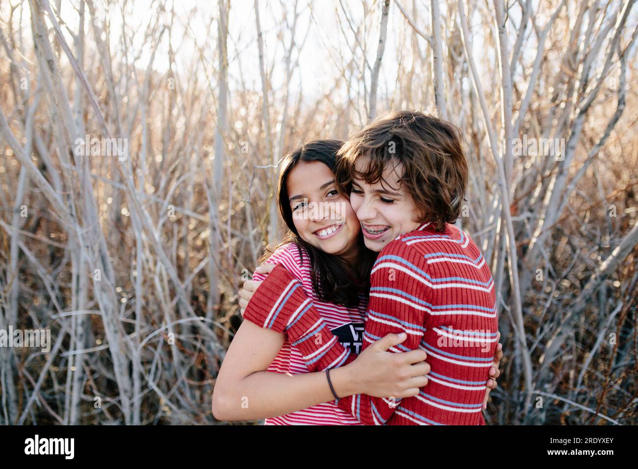 Young teen sisters hug cheek to cheek and smile in a wooded area Stock Photo