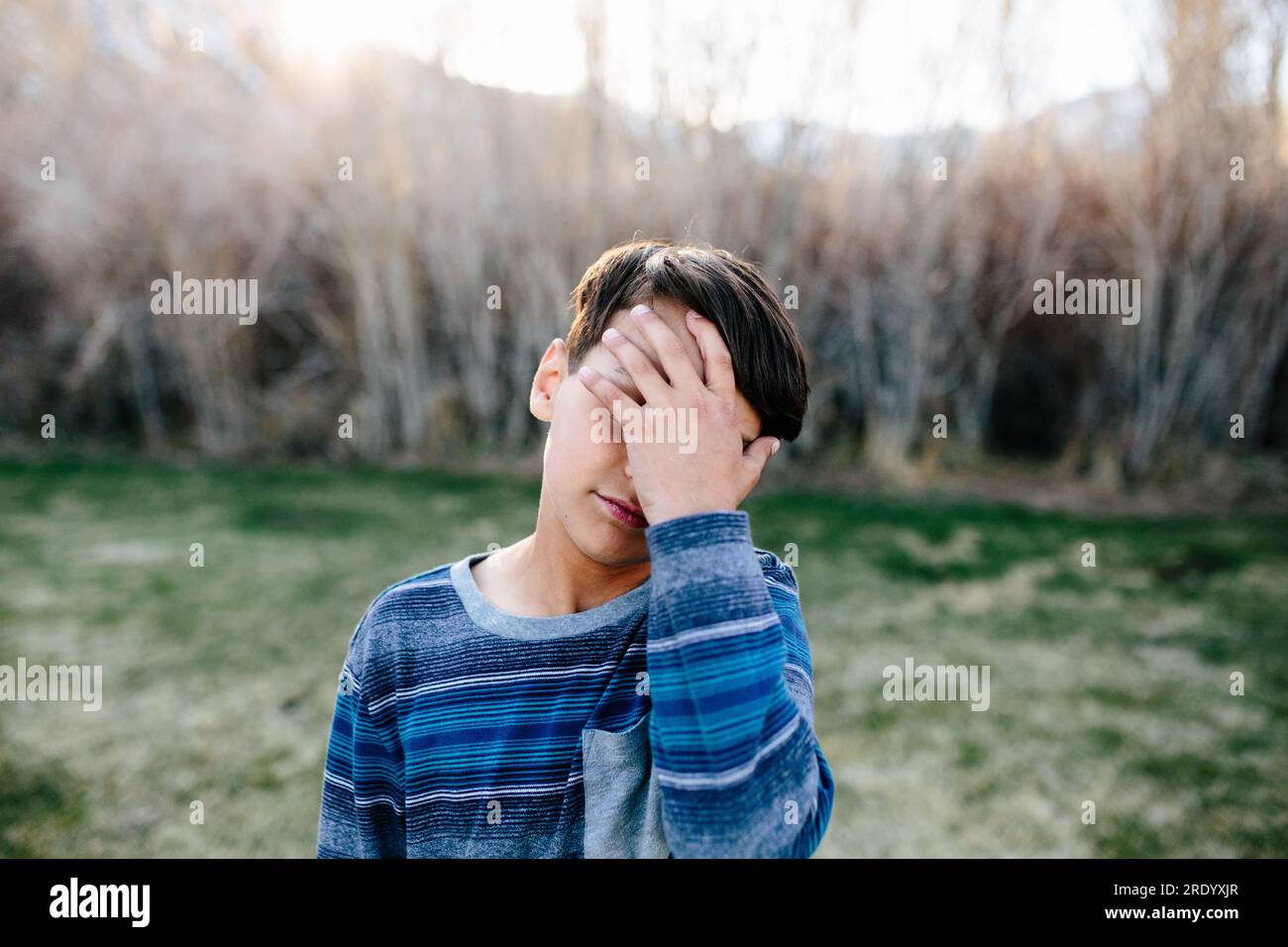 Boy outside appears sad as he covers part of his face with his hand Stock Photo