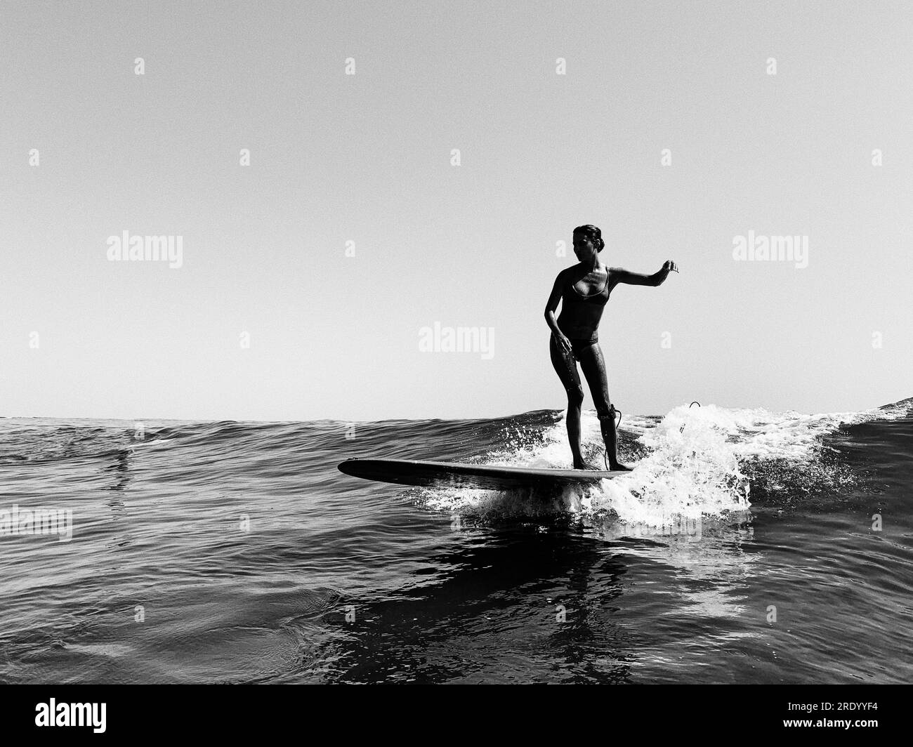 A female surfer in a bikini rides a small wave, black and white Stock Photo