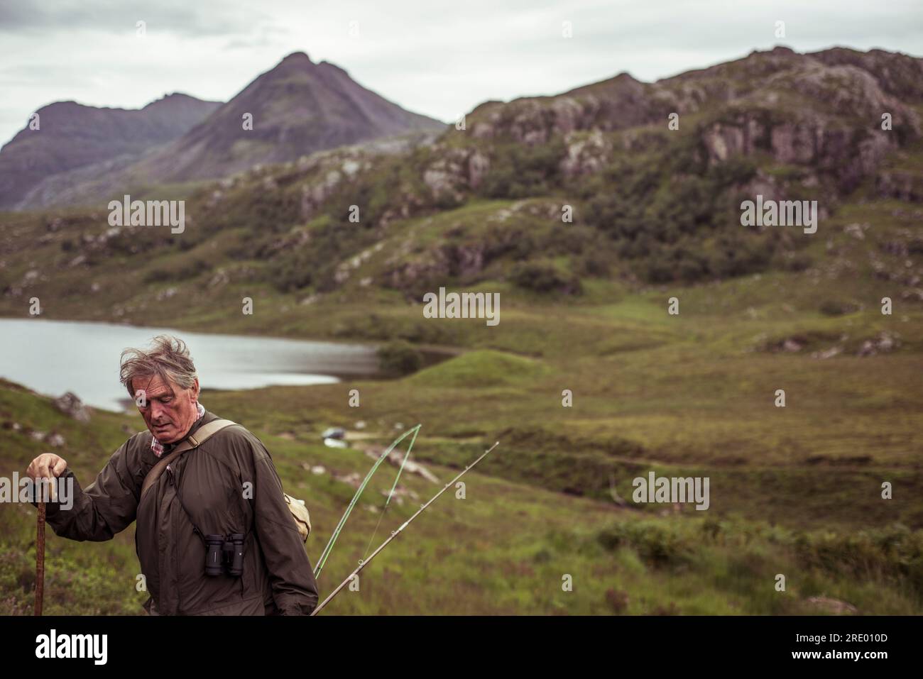 retired man climbs mountain over loch on fishing trip in scotland Stock Photo