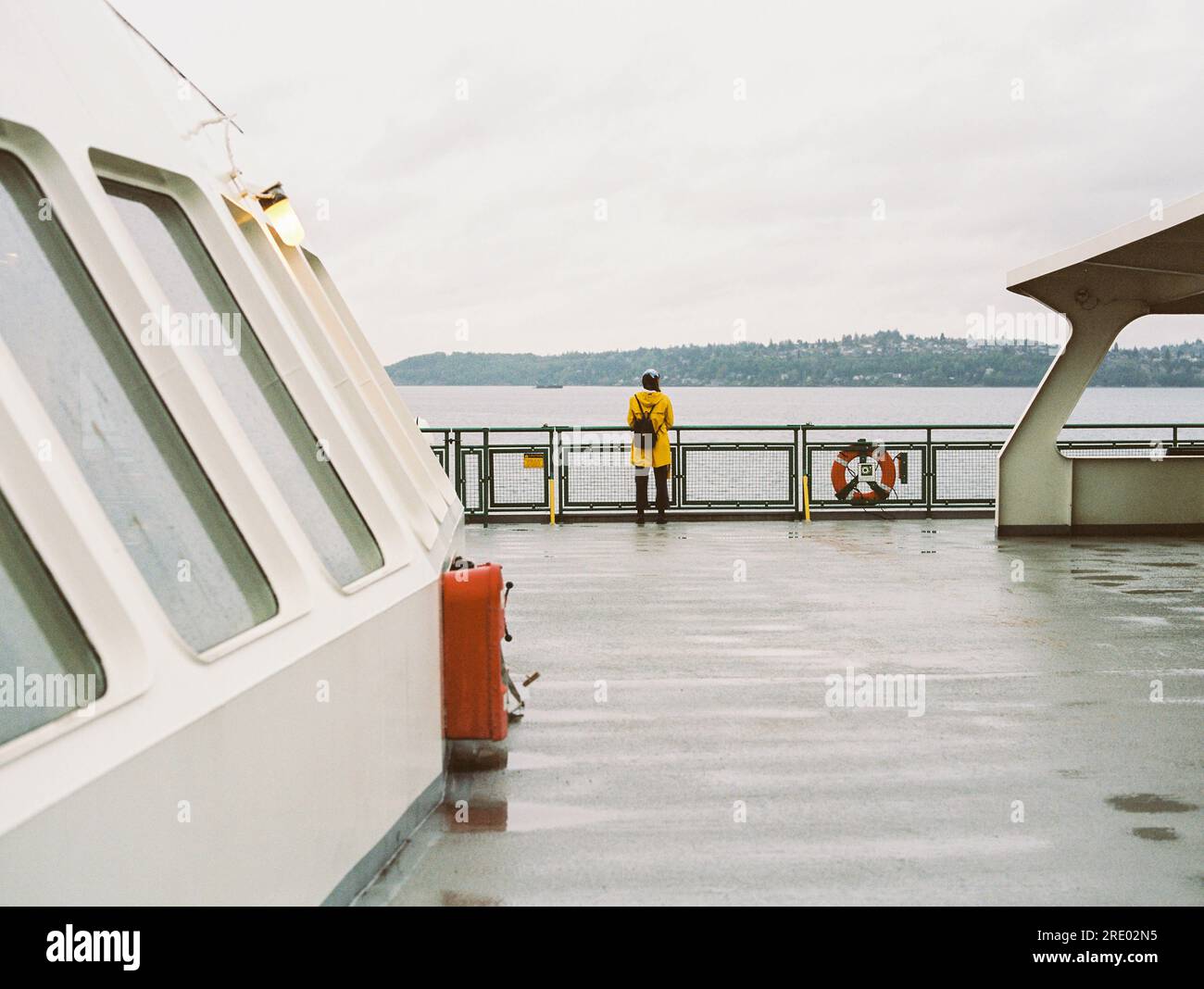 Woman in yellow rain jacket rides ferry in rain, on 35mm film Stock Photo