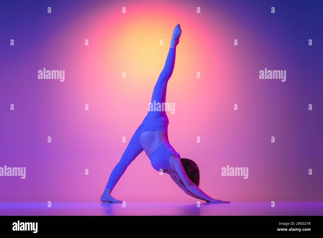 Pregnant woman doing one legged dog pose exercise in neon Stock Photo