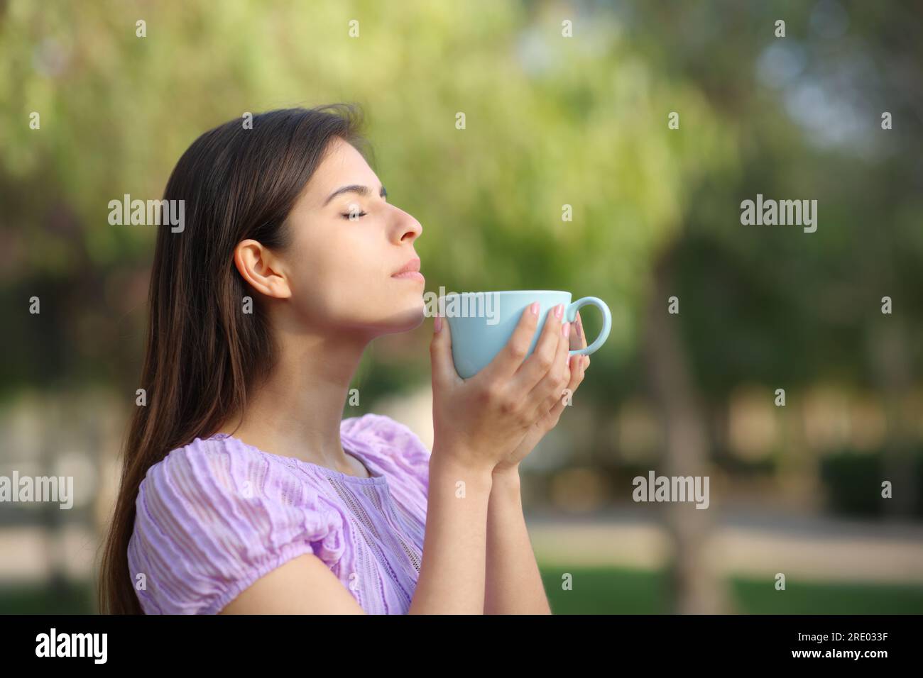 Side view portrait of a woman smelling coffee from mug in a park Stock Photo