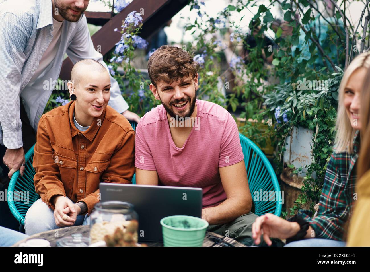 Non-binary individual with shaved head and ear piercing is the focal point of this image, engaging in group study and discussions on a terrace. Stock Photo