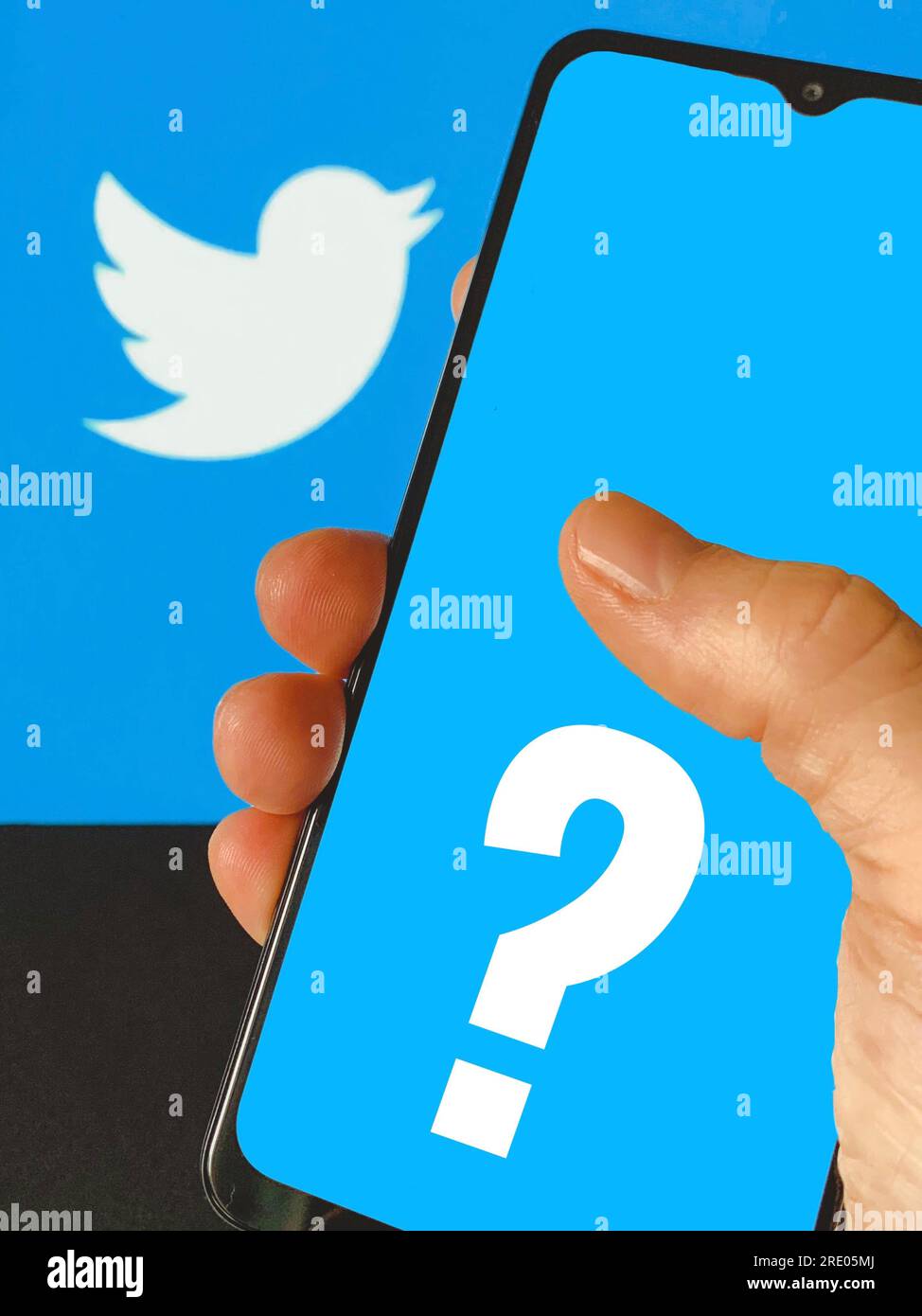 Hand holding mobile device showing twitter logo in the background and a