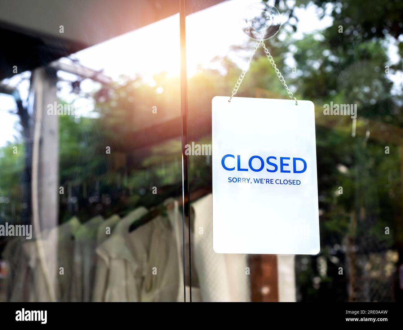 Shop closed, white notice sign with words 'Sorry, we are closed' hanging on glass door in front of the clothing store, small business owner and tempor Stock Photo