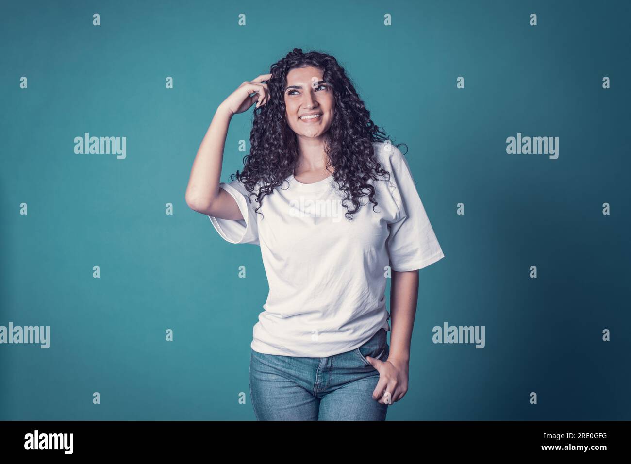 Shot of happy confident curly woman with toothy smile,wears casual basic solid white t-shirt, expresses good emotions, enjoys nice day, thinking isola Stock Photo