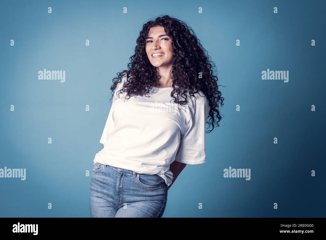 Shot of happy confident curly woman with toothy smile, wears casual basic solid white t-shirt, expresses good emotions, enjoys nice day, isolated over Stock Photo