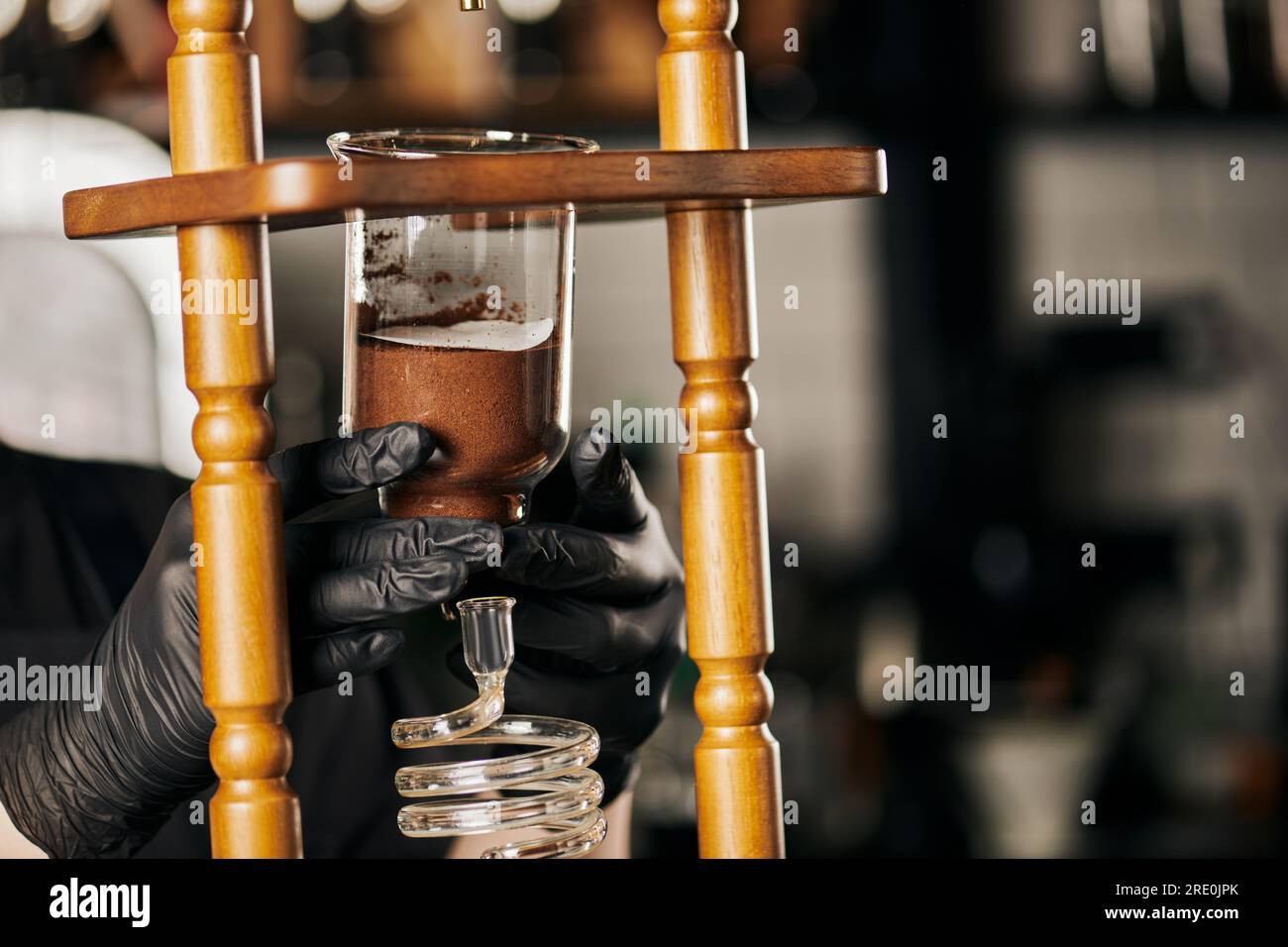 barista in black latex gloves assembling parts of cold drip coffee maker, alternative coffee