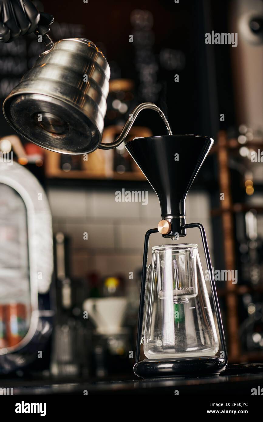 partial view of barista pouring boiling water into assembled siphon