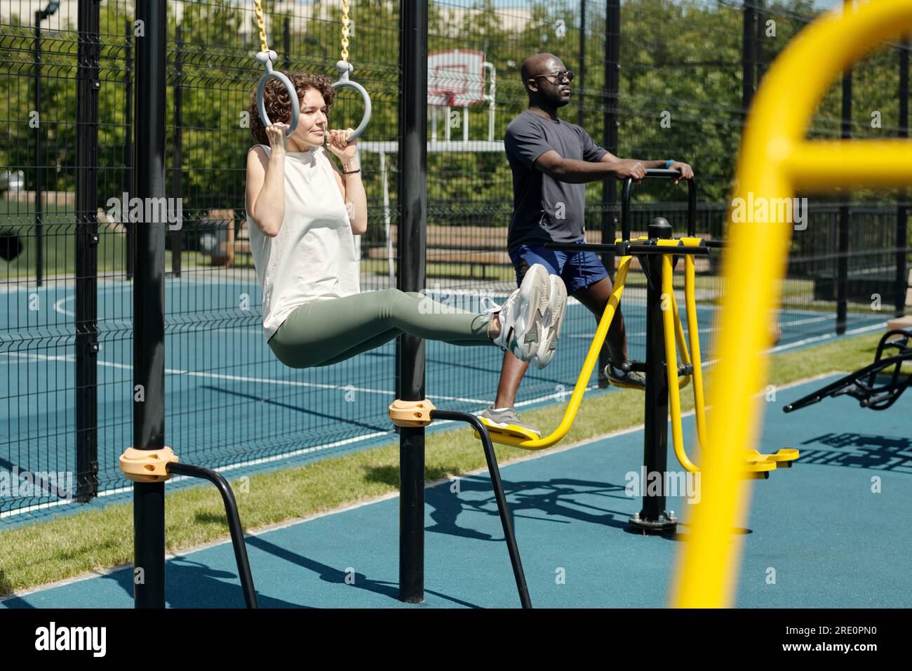 Young brunette sportswoman hanging on still rings and doing L sits on  sports ground against African American man exercising on facilities Stock  Photo - Alamy