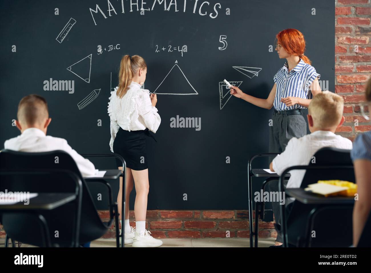 Young woman, teacher of math standing by blackboard with little girl ...