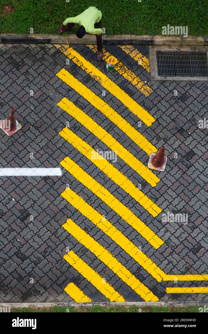Aerial vertical view of a skilled Indian worker is repainting yellow paint on the road bump on the road Stock Photo