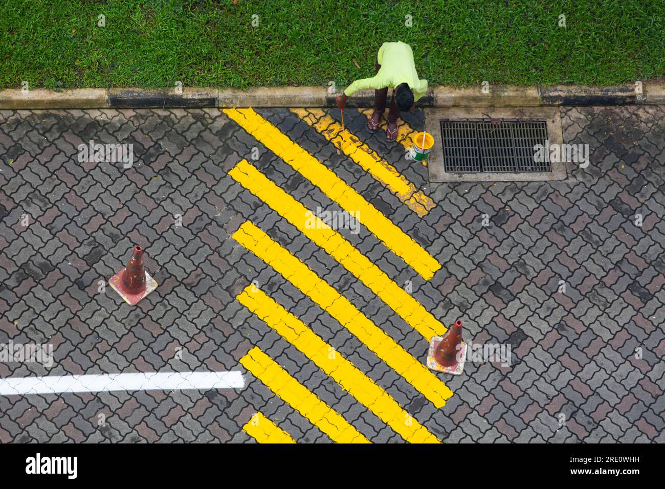 Aerial view of an Indian worker is painting yellow paint on the speed bump on the road. Stock Photo