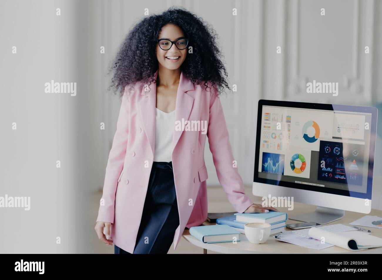 Cheerful African American woman, curly hair, formal outfit, prepares presentation in front of auditorium with computer graphics. Stock Photo
