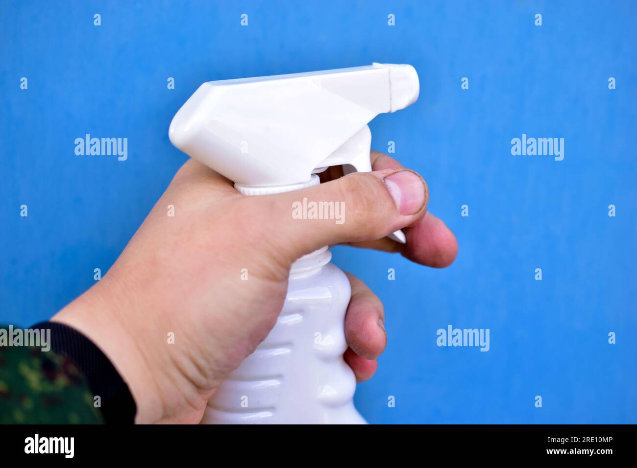 Plastic container with a spray gun in hand on a blue background Stock