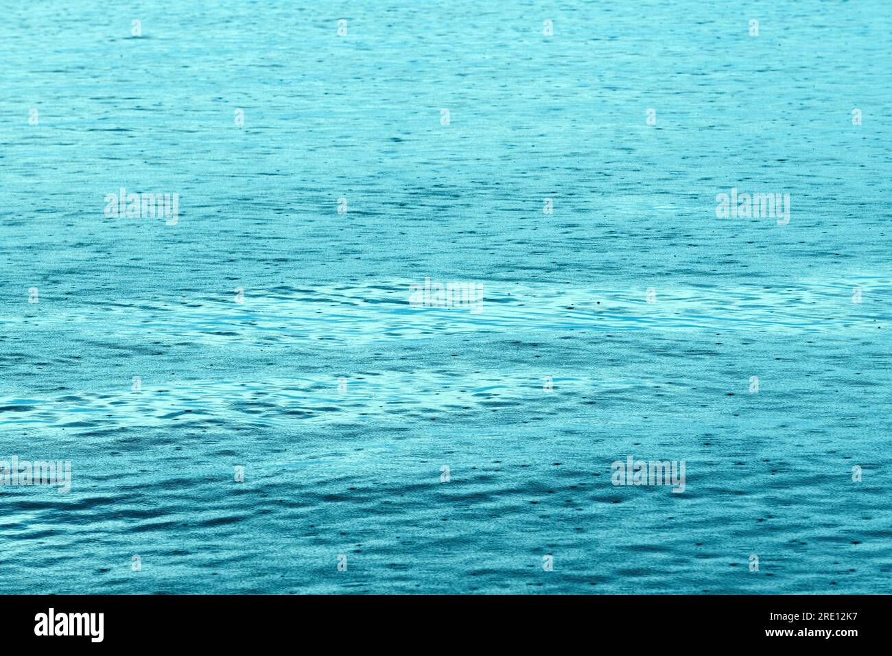 Sudden summer shower rain at seaside, raindrops forming patterns on water surface Stock Photo