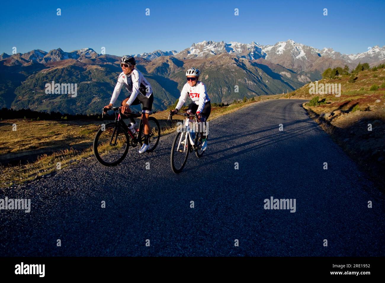 Two cyclists climbing the legendary Col (Granon Pass) in autumn, in the French Alps. Couple of cyclists on a mountain road with a panoramic view of th Stock Photo