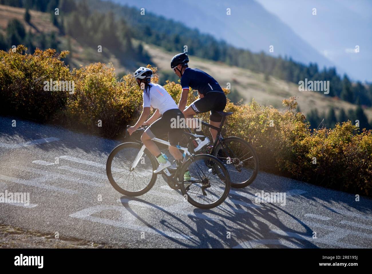 Two cyclists climbing the legendary Col (Granon Pass) in autumn, in the French Alps. Couple of cyclists on a mountain road. Stock Photo