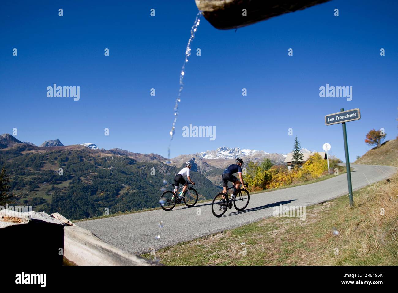 Two cyclists climbing the legendary Col (Granon Pass) in autumn, in the French Alps. Couple of cyclists on a mountain road with a panoramic view of th Stock Photo