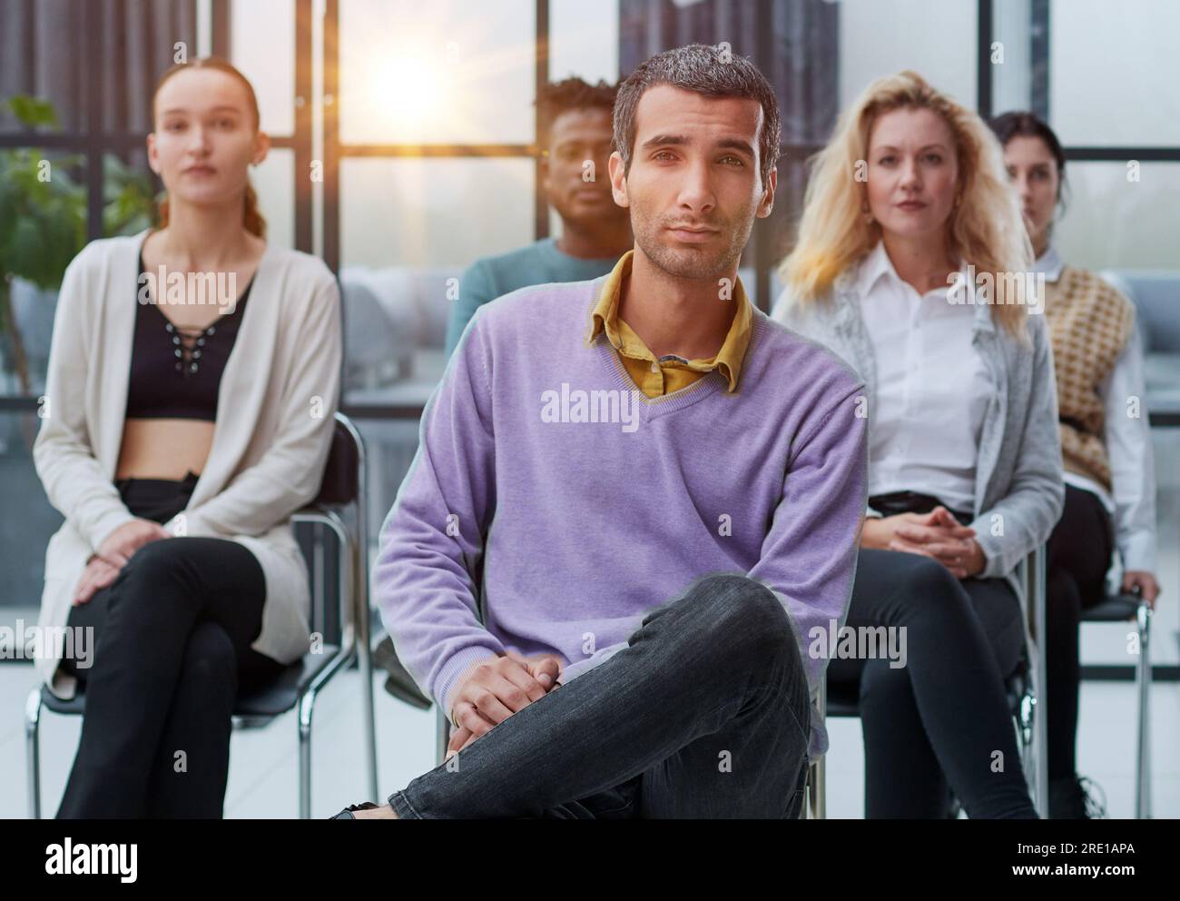 Businessman sitting in front of his colleagues looking at the camera Stock Photo