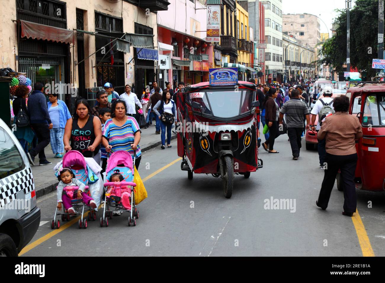 Women pushing girls in pushchairs and motorised tricycle taxi (mototaxi) in commercial market area of central Lima, Peru Stock Photo