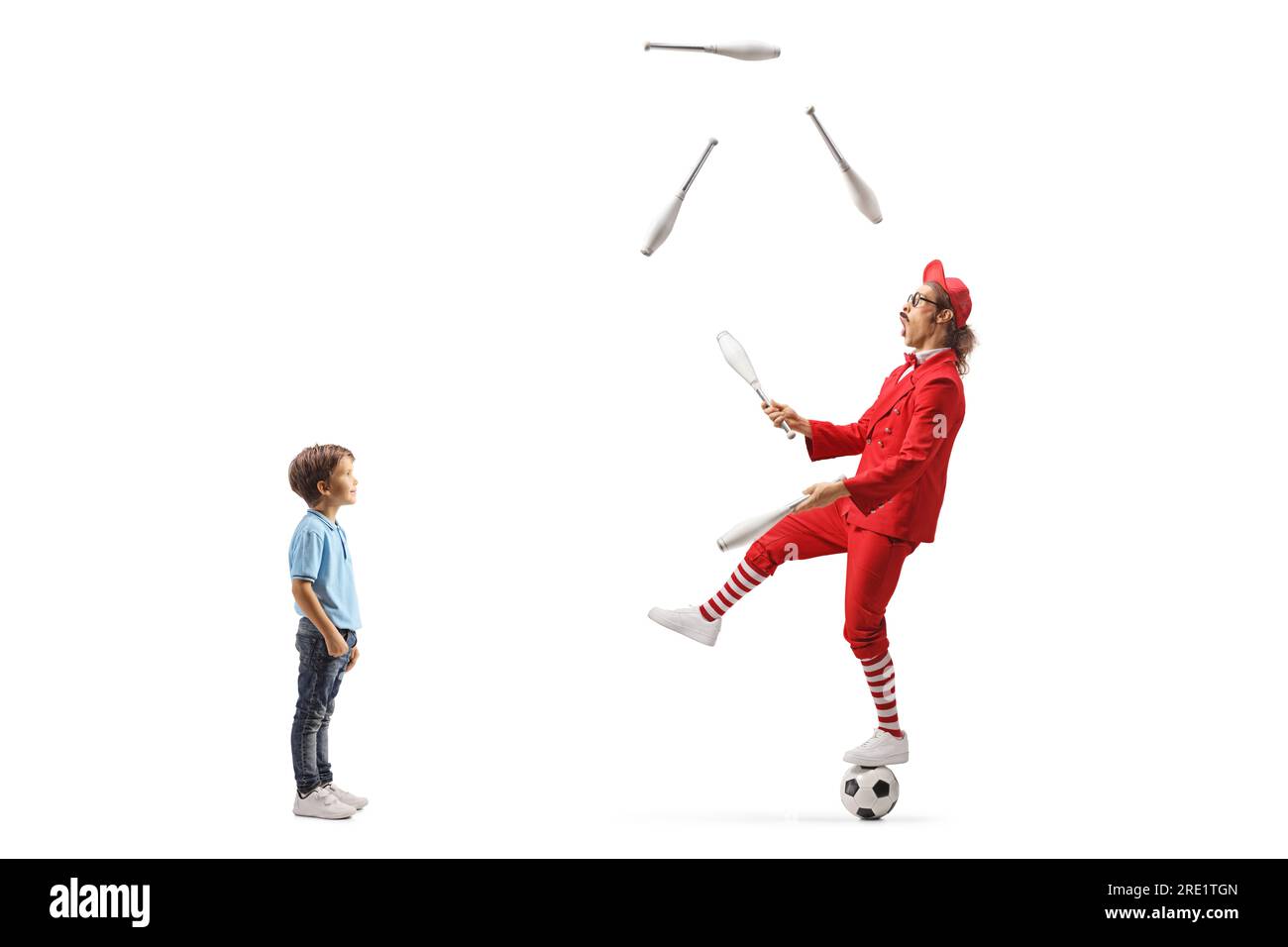 Boy watching a man in a red suit standing on a football and juggling isolated on white background Stock Photo