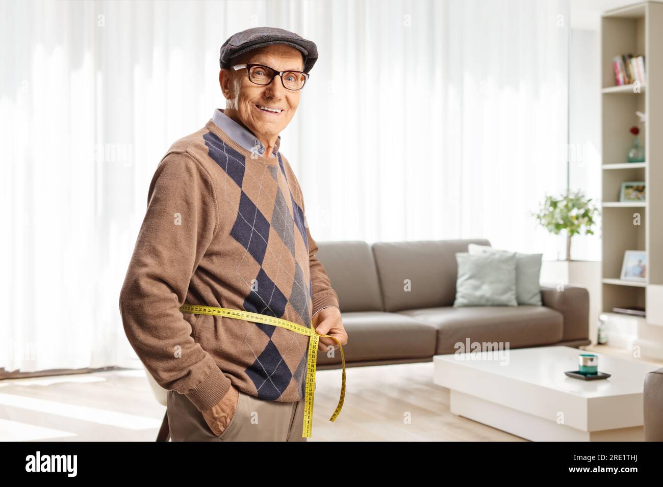 Elderly man measuring waist with a tape inside a living room Stock Photo