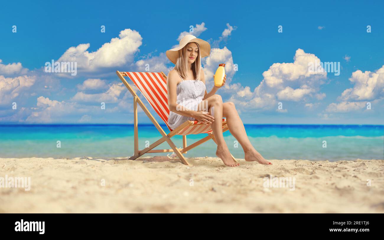 Woman sitting on a deck chair and applying sun cream on legs by the sea Stock Photo