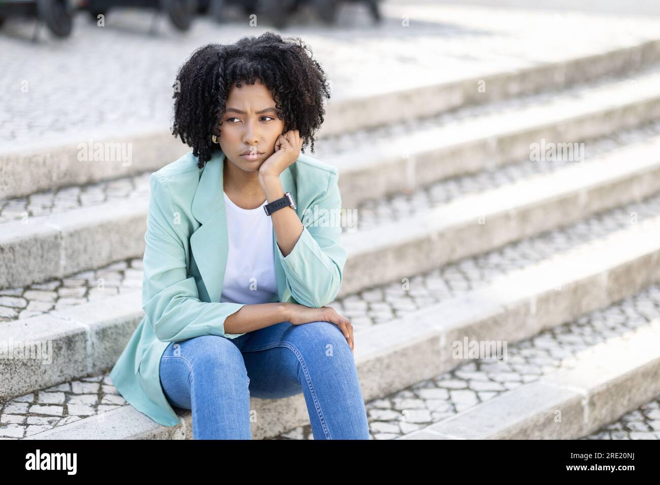 Unhappy frustrated pensive millennial black woman sitting on street Stock Photo